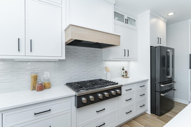 kitchen featuring custom range hood, light wood-style flooring, stainless steel gas stovetop, white cabinets, and high end black fridge
