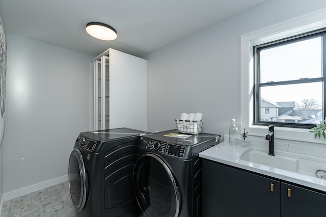 clothes washing area featuring cabinet space, washing machine and dryer, baseboards, and a sink