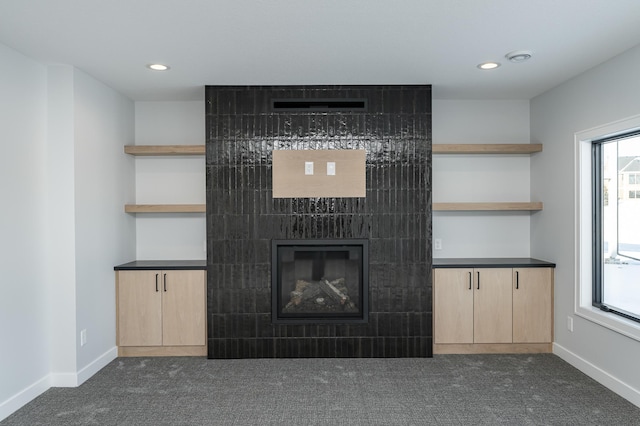 unfurnished living room featuring a wealth of natural light, dark carpet, and a tiled fireplace