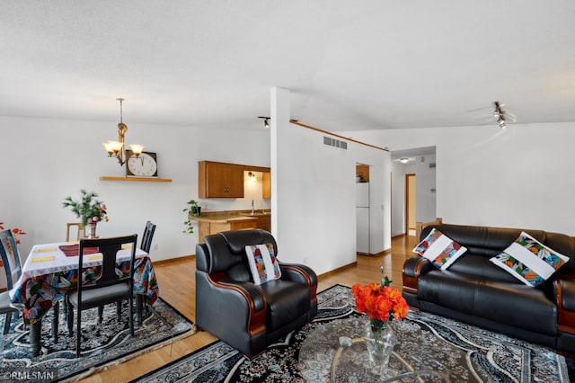 living room featuring vaulted ceiling, sink, a chandelier, and light hardwood / wood-style floors