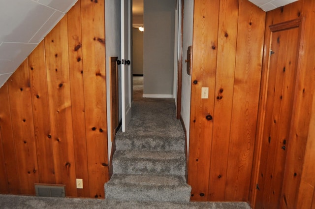 staircase featuring carpet, lofted ceiling, and wooden walls