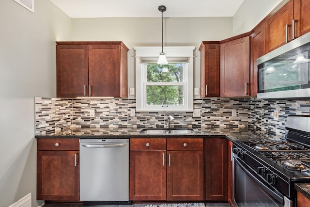 kitchen with appliances with stainless steel finishes, tasteful backsplash, sink, pendant lighting, and dark stone countertops