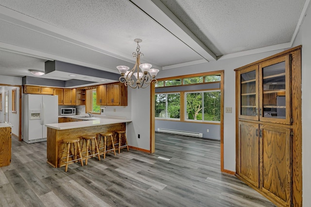 kitchen featuring stainless steel microwave, baseboard heating, a peninsula, white fridge with ice dispenser, and brown cabinetry