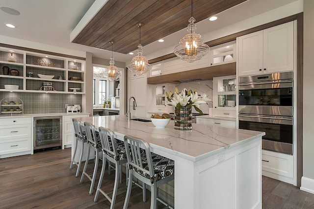 kitchen featuring a center island with sink, white cabinetry, double oven, and beverage cooler