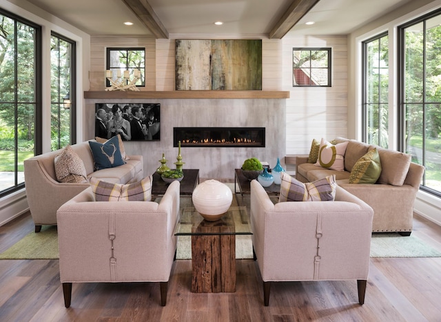 living area featuring a wealth of natural light, beam ceiling, a glass covered fireplace, and wood finished floors