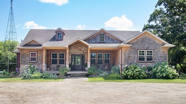 craftsman-style home with stone siding, a porch, and roof with shingles