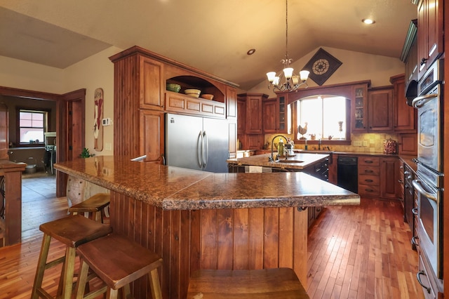 kitchen featuring a breakfast bar, hanging light fixtures, vaulted ceiling, stainless steel built in refrigerator, and open shelves