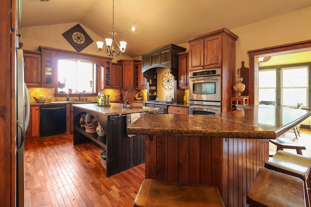 kitchen with appliances with stainless steel finishes, an island with sink, a kitchen bar, and glass insert cabinets