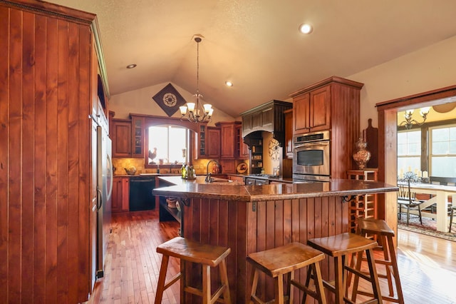 kitchen with lofted ceiling, decorative light fixtures, stainless steel appliances, a sink, and glass insert cabinets