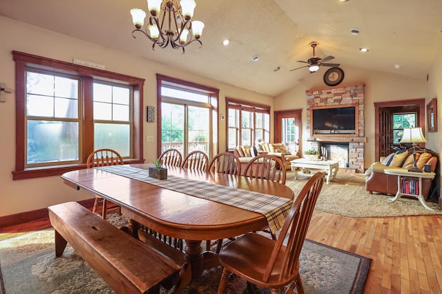 dining space with lofted ceiling, ceiling fan with notable chandelier, a fireplace, wood finished floors, and baseboards