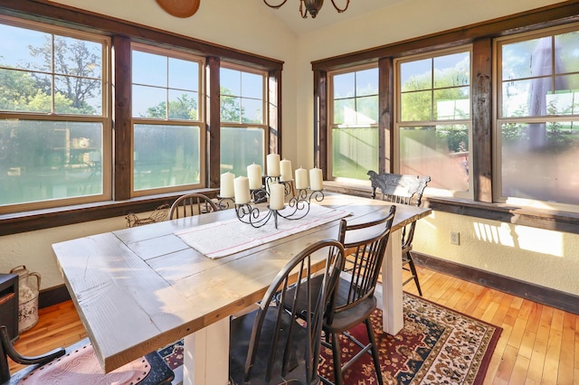 dining area with a chandelier, a wealth of natural light, vaulted ceiling, and wood finished floors