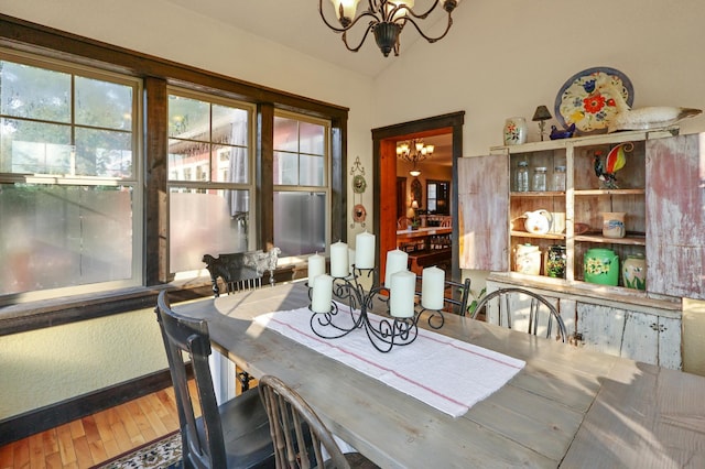 dining area with a chandelier, vaulted ceiling, and wood finished floors