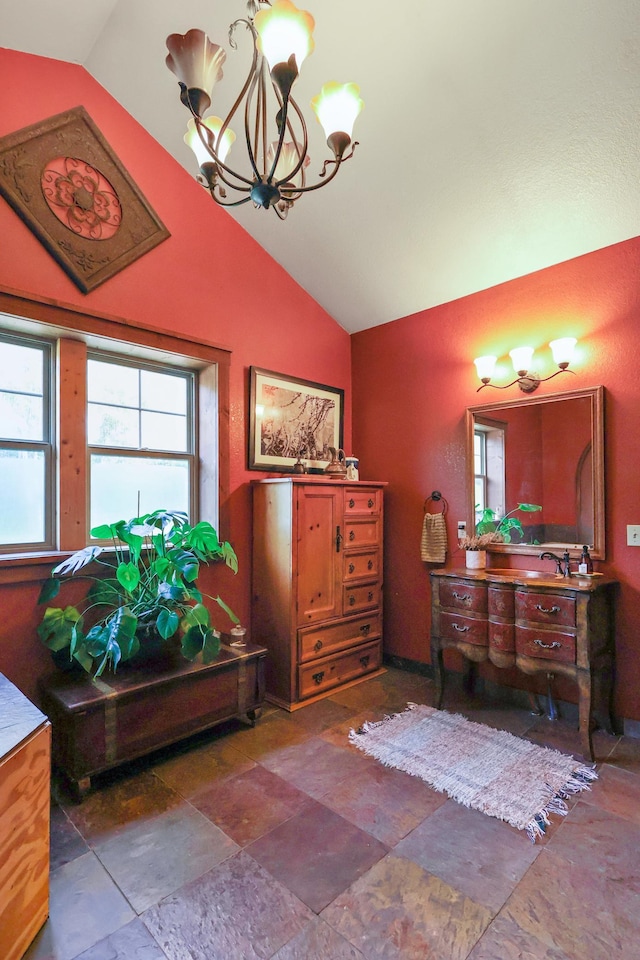 bathroom featuring vaulted ceiling, stone finish flooring, a chandelier, and vanity