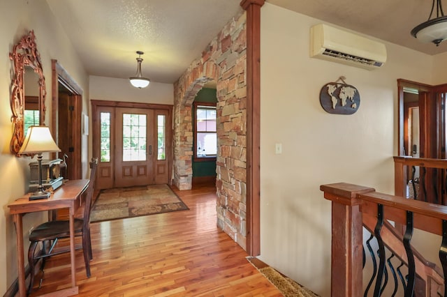 entrance foyer featuring arched walkways, an AC wall unit, light wood-style flooring, and a textured ceiling