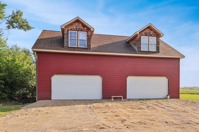 exterior space with a shingled roof, a detached garage, and dirt driveway