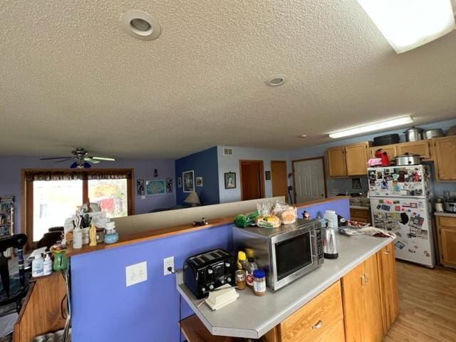 kitchen featuring light wood-type flooring, a textured ceiling, white fridge, and ceiling fan