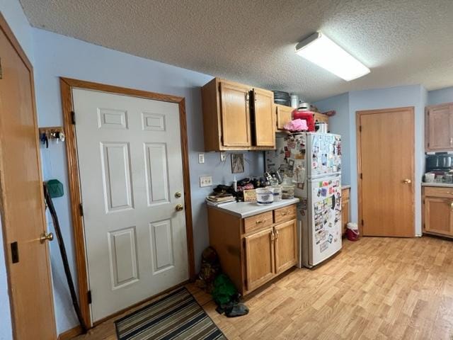 kitchen with light wood-type flooring, a textured ceiling, and white fridge