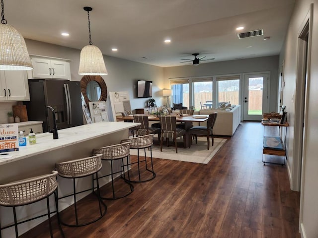kitchen featuring visible vents, a breakfast bar, black refrigerator with ice dispenser, ceiling fan, and dark wood-style flooring