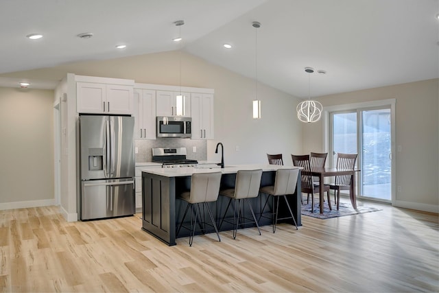 kitchen with a breakfast bar, white cabinets, decorative backsplash, a kitchen island with sink, and stainless steel appliances