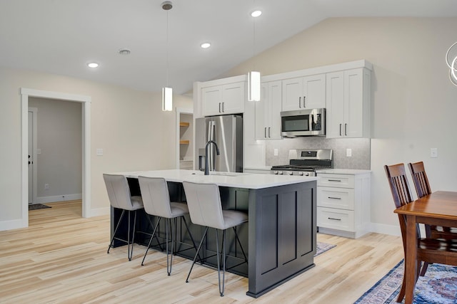 kitchen with appliances with stainless steel finishes, pendant lighting, white cabinetry, lofted ceiling, and a kitchen island with sink