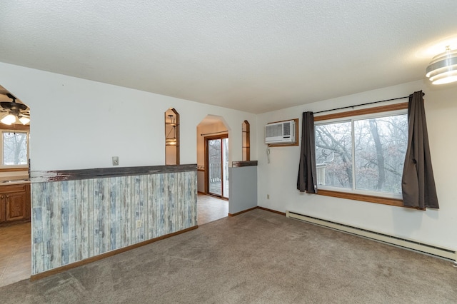 spare room featuring a wall mounted air conditioner, a baseboard heating unit, a textured ceiling, and a healthy amount of sunlight