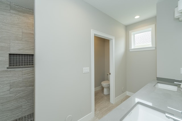 bathroom featuring wood-type flooring, vanity, toilet, and tiled shower