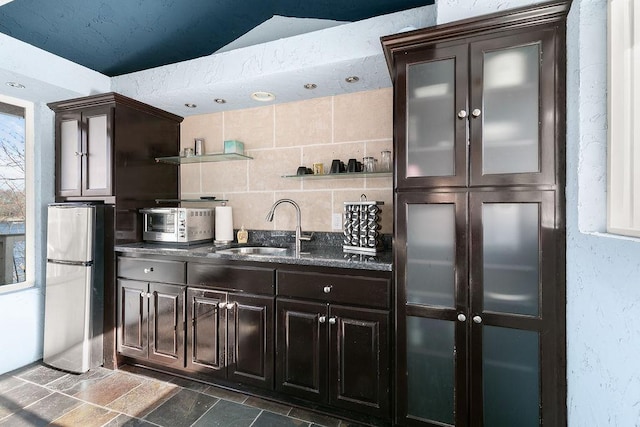 kitchen with lofted ceiling, stainless steel fridge, sink, dark brown cabinets, and decorative backsplash