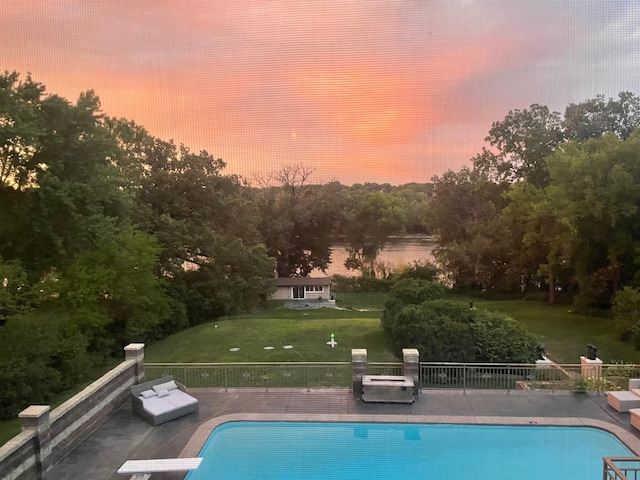 pool at dusk with a patio and a lawn