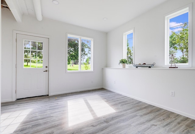 empty room featuring beamed ceiling, a healthy amount of sunlight, and light wood-type flooring