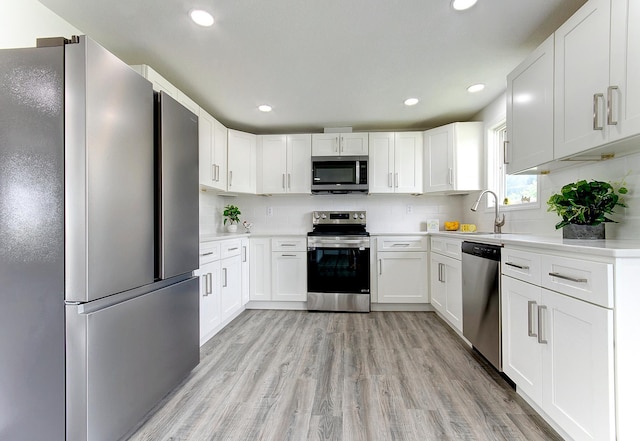 kitchen with backsplash, white cabinets, sink, light wood-type flooring, and appliances with stainless steel finishes