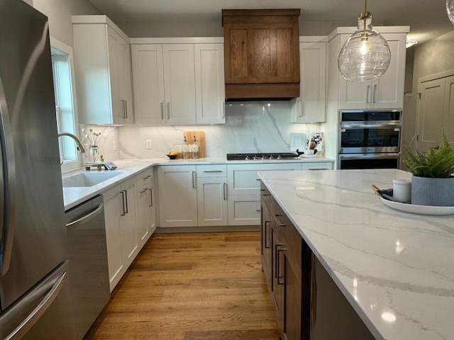 kitchen featuring stainless steel appliances, light stone counters, pendant lighting, decorative backsplash, and white cabinets