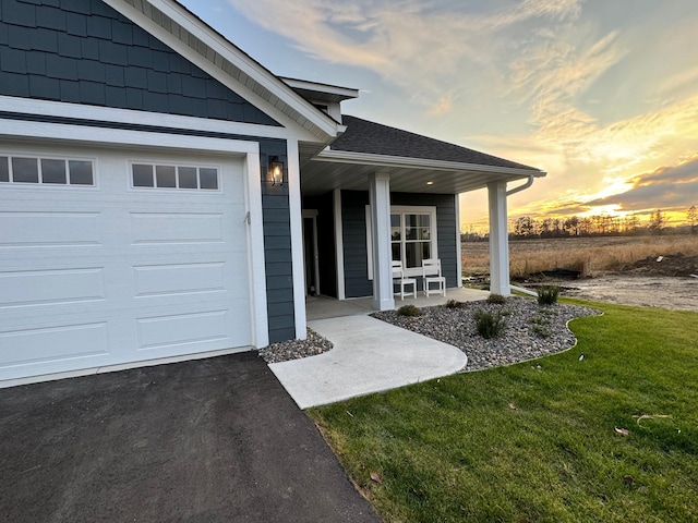 exterior entry at dusk featuring a yard, a porch, and a garage