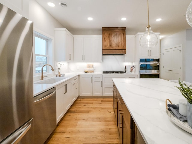 kitchen with light wood finished floors, light stone countertops, stainless steel appliances, white cabinetry, and a sink