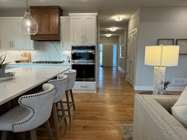 kitchen featuring light stone counters, light wood-style flooring, appliances with stainless steel finishes, a kitchen breakfast bar, and backsplash