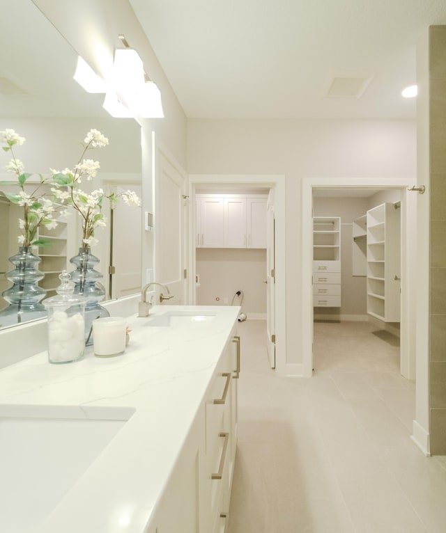 full bathroom featuring a spacious closet, double vanity, baseboards, and a sink