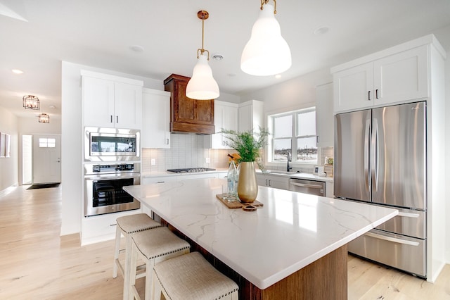 kitchen featuring light stone counters, tasteful backsplash, appliances with stainless steel finishes, and light wood-style flooring