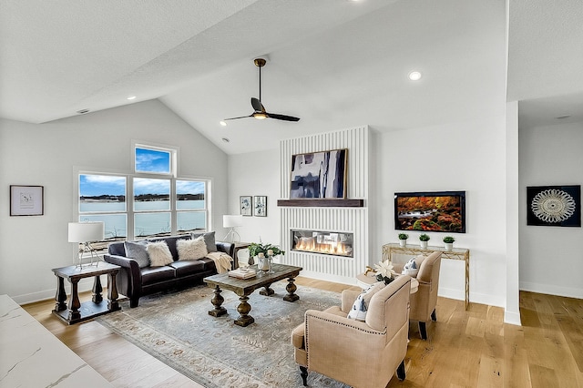 living room featuring a glass covered fireplace, light wood-style flooring, baseboards, and a water view