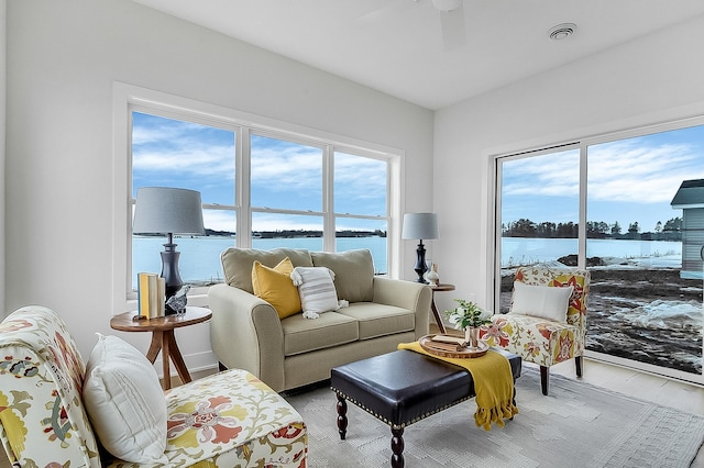 living area with visible vents, a water view, and a healthy amount of sunlight