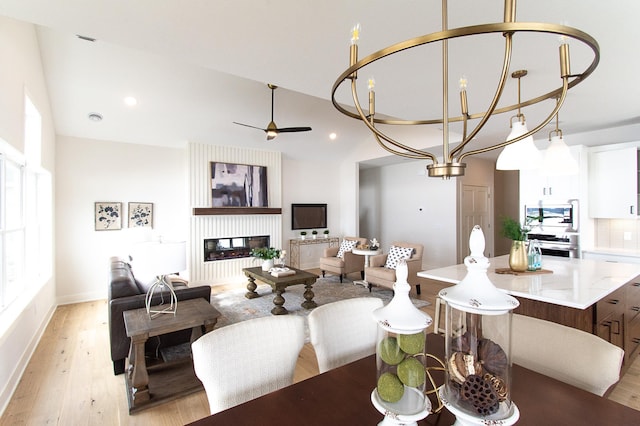 dining area with light wood finished floors, a glass covered fireplace, recessed lighting, and lofted ceiling