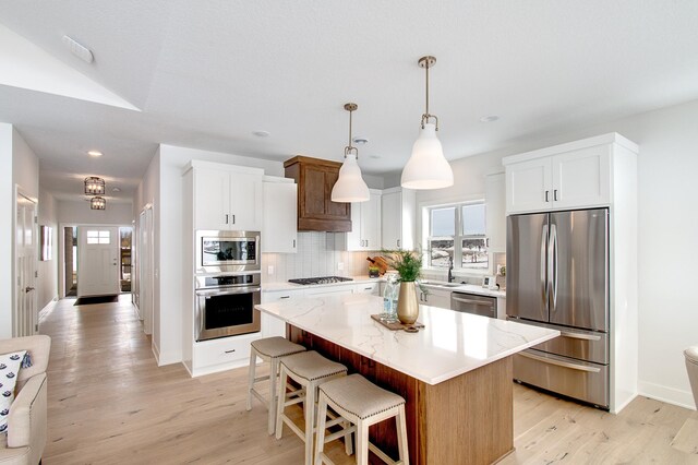 kitchen with decorative backsplash, light wood-style floors, a kitchen island, and stainless steel appliances