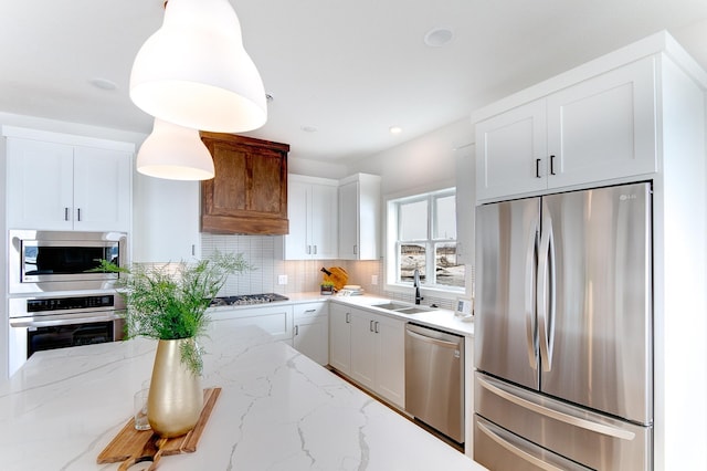 kitchen with tasteful backsplash, light stone counters, appliances with stainless steel finishes, white cabinetry, and a sink