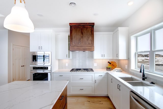 kitchen with a sink, backsplash, stainless steel appliances, light wood finished floors, and custom exhaust hood