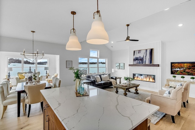 kitchen with light wood-type flooring, pendant lighting, light stone counters, a glass covered fireplace, and open floor plan