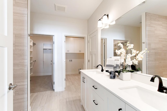 full bath with double vanity, visible vents, a walk in closet, and a sink