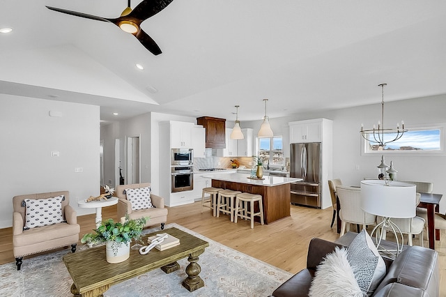 living area with light wood finished floors, recessed lighting, ceiling fan with notable chandelier, and vaulted ceiling