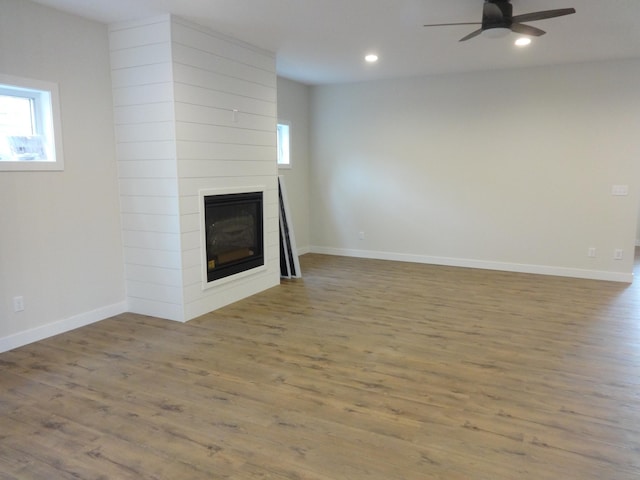 unfurnished living room with a healthy amount of sunlight, a fireplace, ceiling fan, and wood finished floors