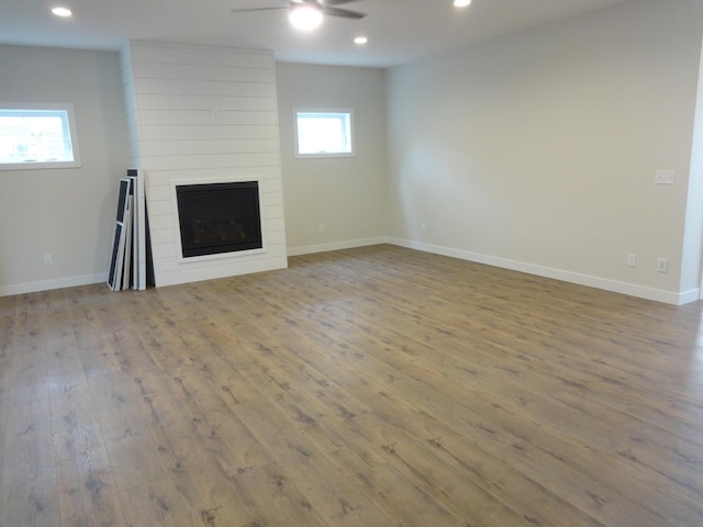 unfurnished living room featuring wood finished floors, plenty of natural light, a ceiling fan, and a large fireplace