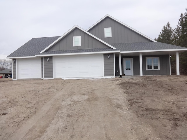 view of front of house with a garage, dirt driveway, and a shingled roof