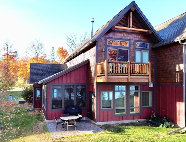 back of property with board and batten siding, roof with shingles, a patio, and a lawn