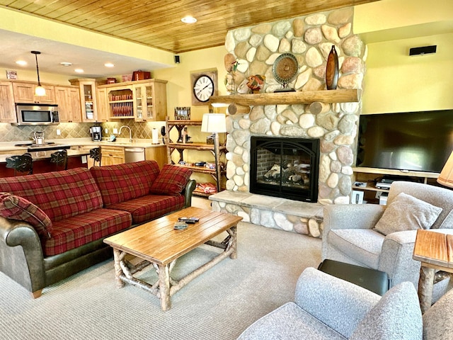 living room with wood ceiling, a stone fireplace, sink, and light colored carpet